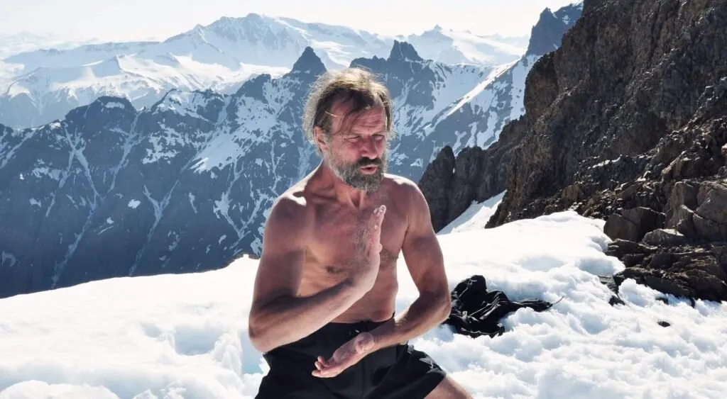 Wim Hof sitting shirtless in the snow beneath mountain peaks
