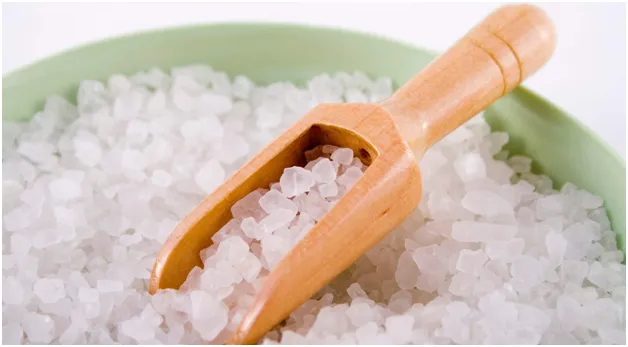 A wooden scoop resting in a bowl of coarse bath-salt crystals