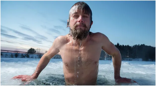 A shirtless man rising out of an icy lake, water streaming from his hair and beard