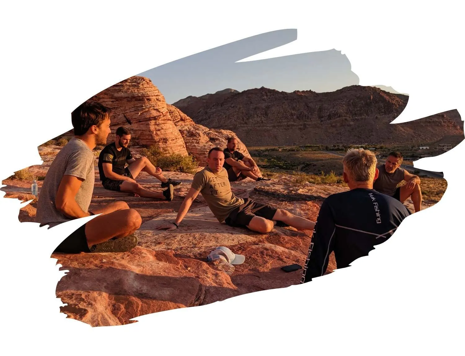 A group sitting together on red desert rocks at sunset, shown in a brush-stroke frame